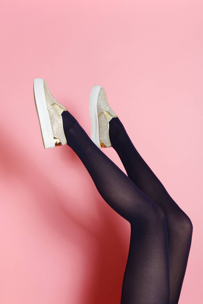 Legs of young caucasian woman in black tights and golden shoes on pink background - Zdjęcie, obraz