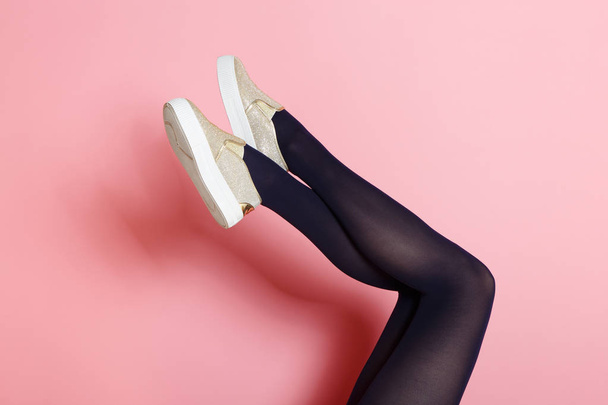 Legs of young caucasian woman in black tights and golden shoes on pink background - Фото, зображення