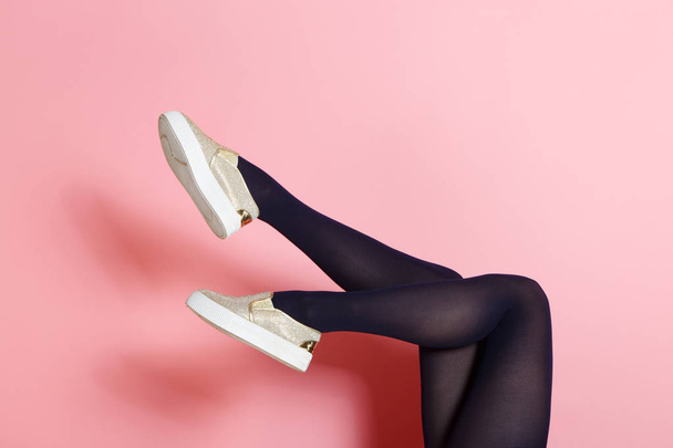 Legs of young caucasian woman in black tights and golden shoes on pink background - Fotoğraf, Görsel