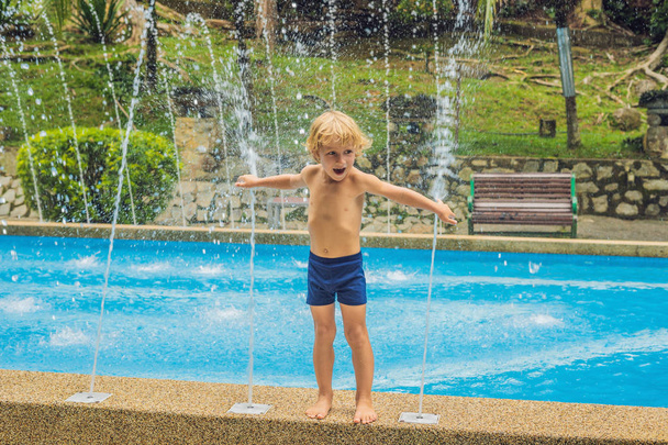 Niño feliz jugando con la fuente de agua en la piscina
 - Foto, imagen