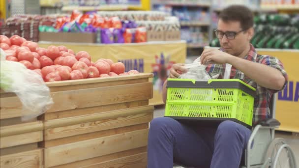 Man met een handicap in een rolstoel winkelen in de supermarkt kiest de tomaten en zet ze in een package.close omhoog - Video