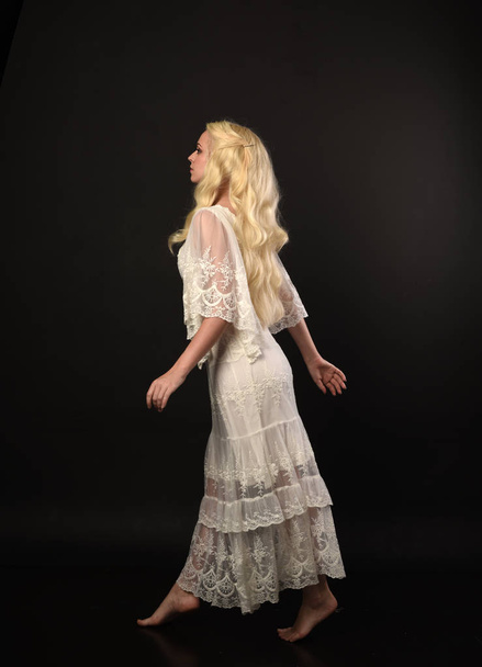 повнометражний портрет блондинки в білій мереживної сукні. стоїть поза спиною до камери. чорний студійний фон
. - Фото, зображення