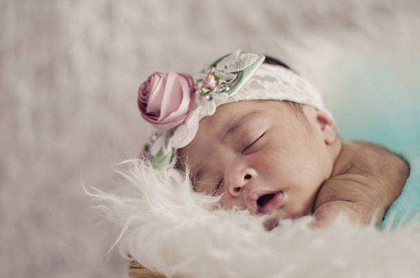 portrait of cute and adorable newborn baby with floral head band sleeping in basket covered with furry mat.motherhood and parenting concept. - Photo, image