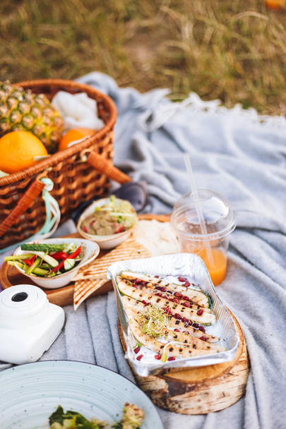 Закрыть пикник с разнообразием вкусной еды и корзины с фруктами на одеяло для пикника в парке
  - Фото, изображение