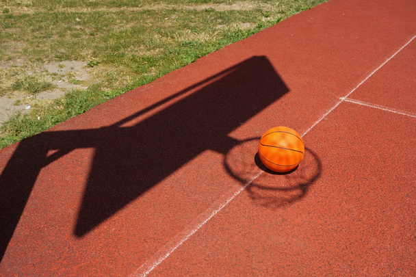 Basketball on a court placed inside the shadow of the net and goalpost in a conceptual image with copy space - Photo, image