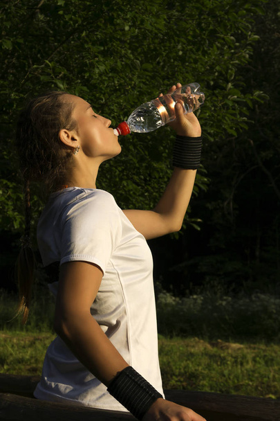 meisje na het sporten in het park blussen Dorst drinkt water uit de fles - Foto, afbeelding