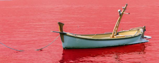 Um velho barco de pesca de madeira ancorado em um pequeno porto no fundo vermelho
 - Foto, Imagem