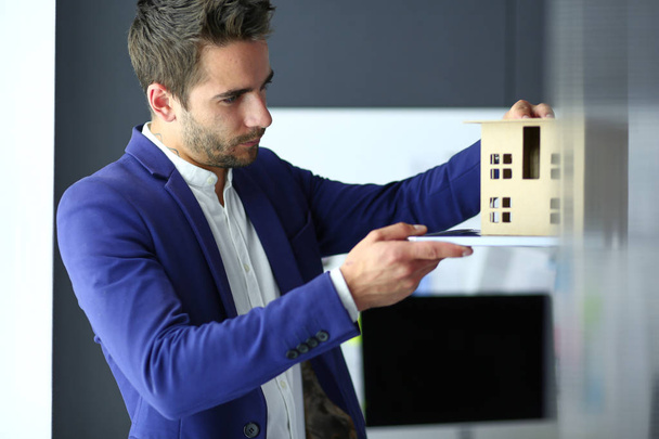Homme d'affaires tenant maison miniature à portée de main debout dans le bureau
. - Photo, image