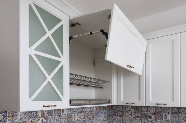 Kitchen cabinet with opened fronts with dish holder shelves inside. Lift system for bi-fold fronts for direct access in kitchen cabinets. Kitchen in a neoclassical style with wooden white fronts.  - Photo, Image