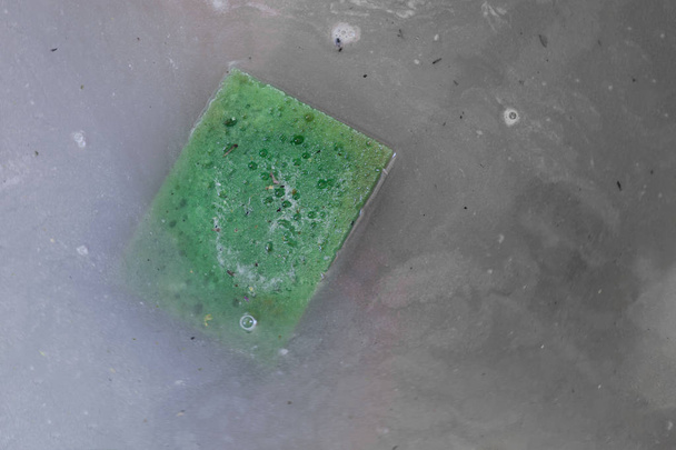 Groene vuile spons drijvend in vuile grijs water - Foto, afbeelding