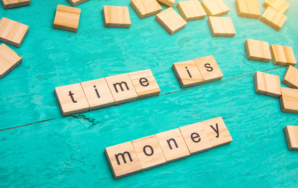 Čas jsou peníze slova vykládané dřevěné písmena abecedy konceptu na modrém pozadí - Fotografie, Obrázek