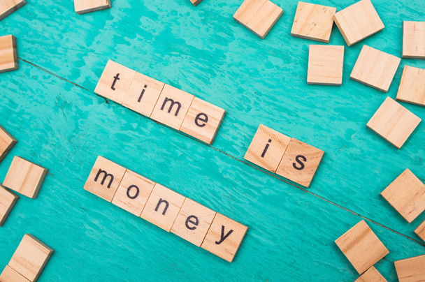 Time is money words laid out with wooden letters of the alphabet concept on a blue background - 写真・画像