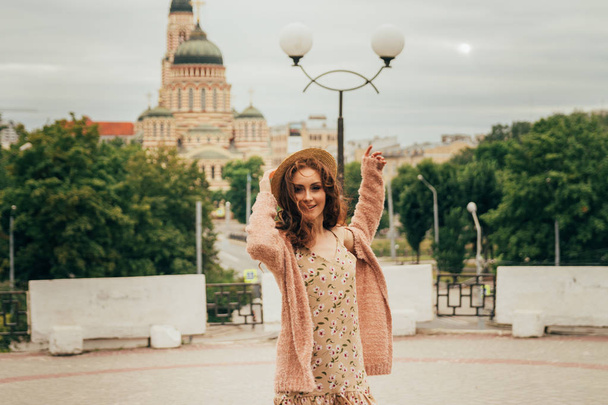 A romantic girl in the city wearing a dress and a sweater of warm colors, her hair develops in the wind. smiling and dizzy. keeps his hat on - Foto, Imagem