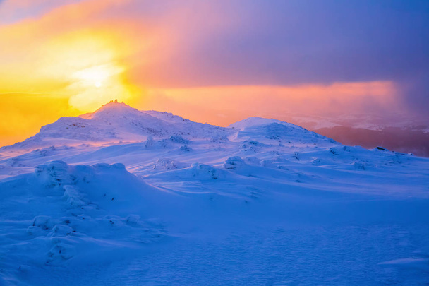 Sunrise enlightens sky, mountain and trees standing in snowdrifts covered by frozen snow with yellow shine. - Fotó, kép