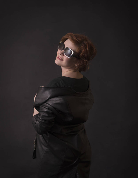 Emotional brunette posing in the Studio in a leather cloak.Isolated image on a dark background. - Φωτογραφία, εικόνα