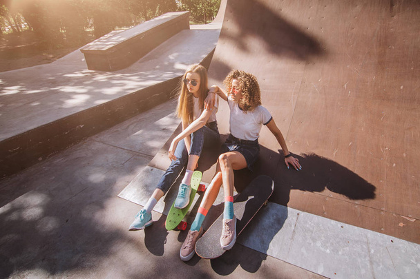 Deux amies patineuses assises sur la rampe et traînant au skate park. Rire et s'amuser
. - Photo, image