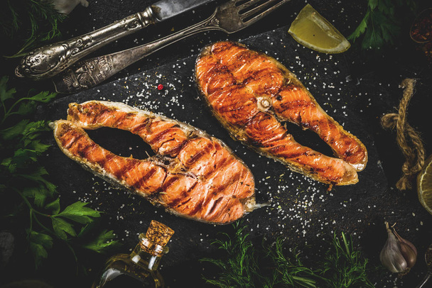 Grilovaný losos ryby steaky s ingrediencí citronem, bylinky, olivový olej, břidlicové prkénko, tmavě rezavé pozadí kopie prostor - Fotografie, Obrázek