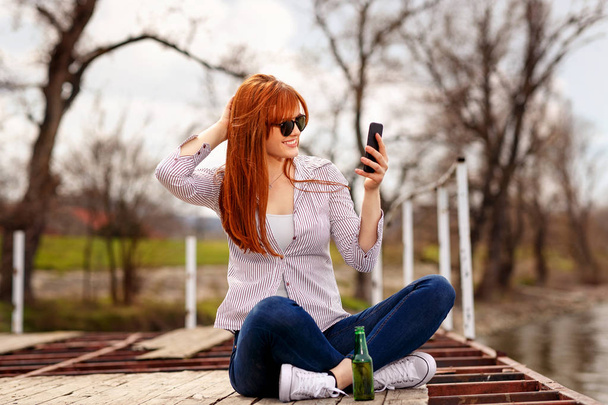 Smiling girl enjoying and relaxing out in nature and taking selfie by the river - Фото, изображение