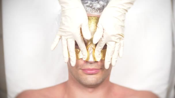 Terapia de spa para homens bonitos recebendo máscara facial. 4K. Movimento lento. Recepção de um cosmetologista. máscara dourada
 - Filmagem, Vídeo