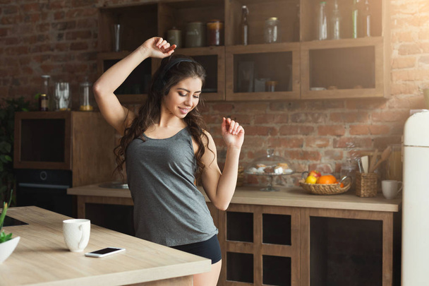 Happy young woman listening music in kitchen - Foto, Imagen