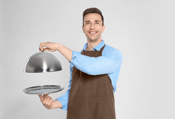 Handsome waiter holding metal tray with lid on light background - Foto, Bild