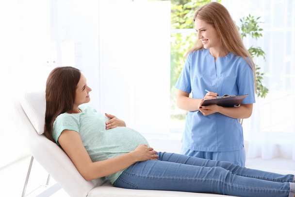 Young pregnant woman with her doctor in clinic - Фото, изображение