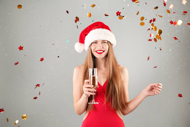 Young beautiful woman in Santa hat and swimsuit holding glass of champagne on grey background. Christmas celebration - Fotó, kép