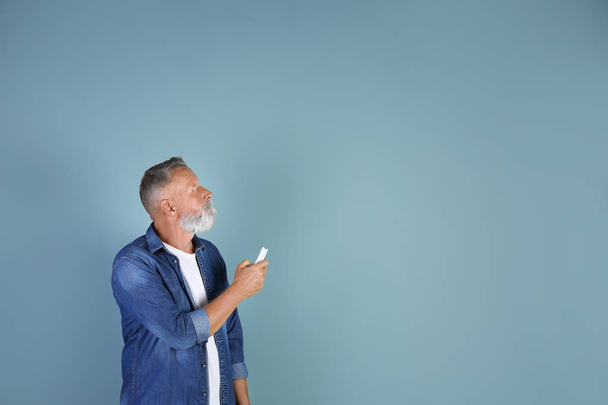 Senior man with air conditioner remote control on color background - Фото, изображение