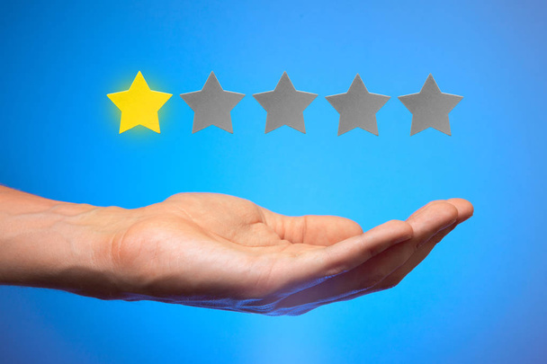 One golden yellow stars out of five. Man holds star on the palm of his hand, puts rating, reviews - Photo, Image
