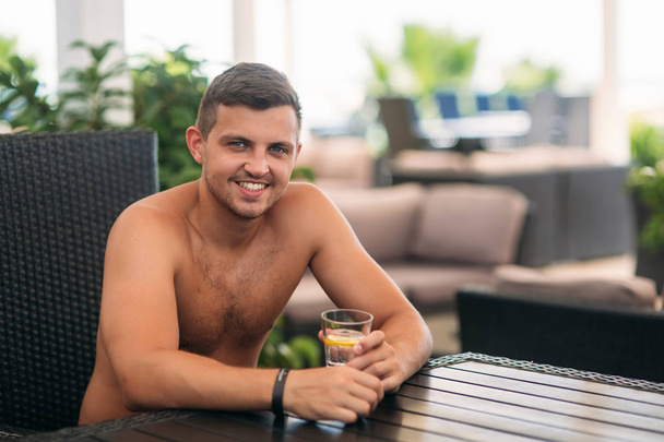 Young man sitting of the beach club bar and drinking tonic - Zdjęcie, obraz