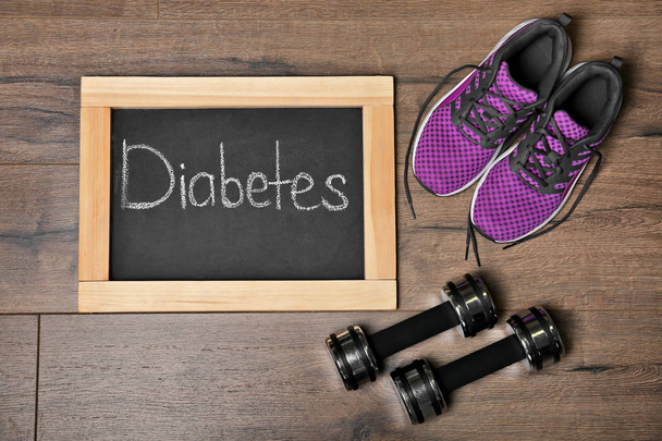Flat lay composition with word DIABETES, sneakers and dumbbells on wooden background - Photo, Image