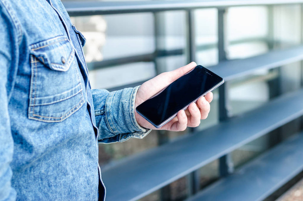スタイリッシュな服を着て近くを流行に敏感なビジネス男を使用してスマート携帯電話アプリ屋外黒 Oled ディスプレイ背景デニム ジーンズ シャツ - 写真・画像