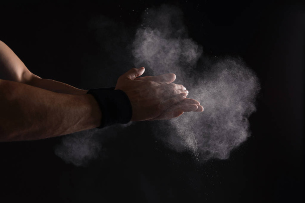 Young man applying chalk powder on hands against dark background - Photo, image