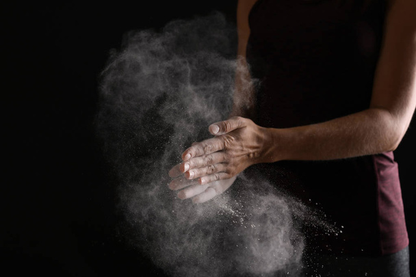 Young woman applying chalk powder on hands against dark background - Foto, Imagen