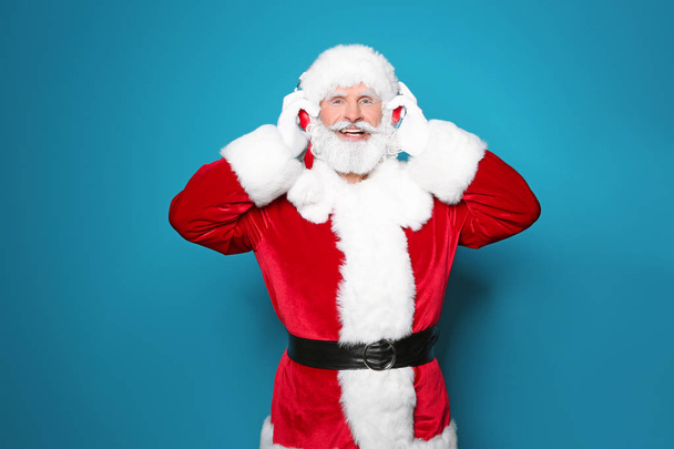 Santa Claus listening to Christmas music on color background - Фото, зображення