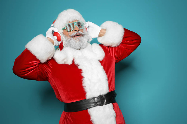 Santa Claus listening to Christmas music on color background - Foto, afbeelding