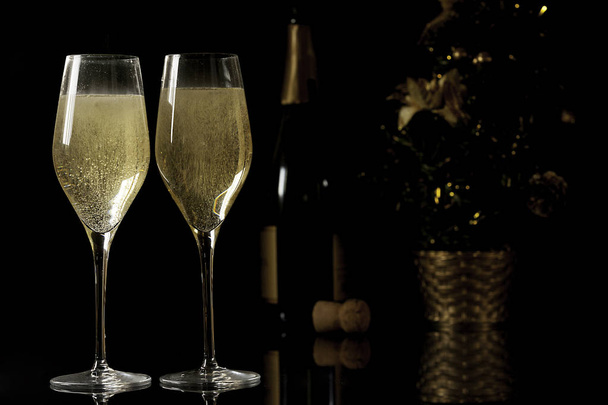 Two champagne glasses, champagne bottle and Christmas tree on black background  - Photo, Image