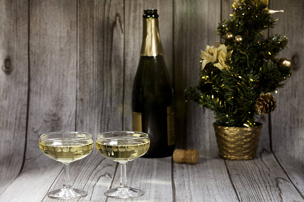 Two champagne glasses, champagne bottle and Christmas tree on wood  background  - Photo, Image