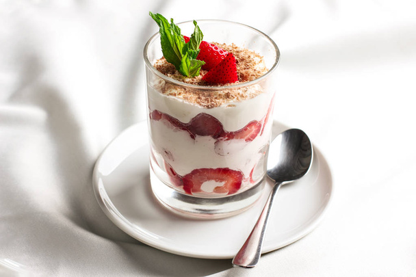 Gezonde dessert in glas met verse aardbeien en room yoghurt op witte achtergrond - Foto, afbeelding