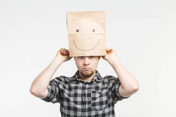 Hombres tristes quitándose la máscara de papel feliz sobre fondo blanco
 - Foto, Imagen