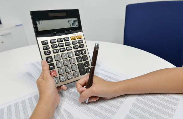 La mano de la mujer está usando la calculadora para calcular el documento financiero
 - Foto, Imagen