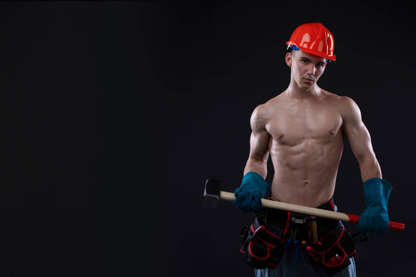 Knappe jonge topless bouwvakker in helm met sledge hammer, studio opname, zwarte achtergrond. bouwer. Kopiëren van ruimte - Foto, afbeelding