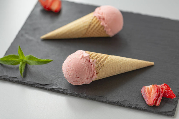 Crème glacée aux fraises dans un cône de gaufre sur une plaque d'ardoise
 - Photo, image