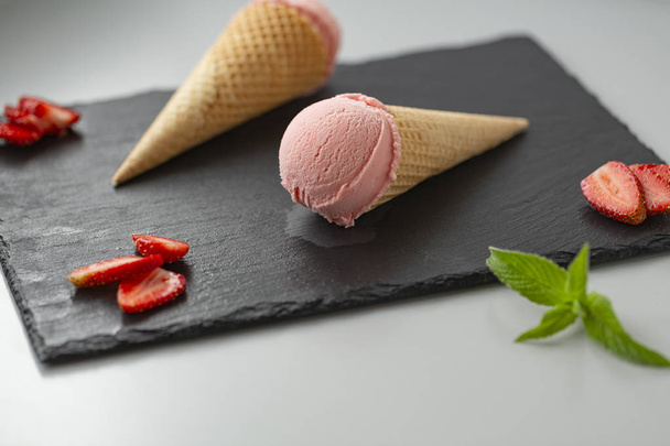 Strawberry ice cream in a waffle cone on a slate plate - 写真・画像
