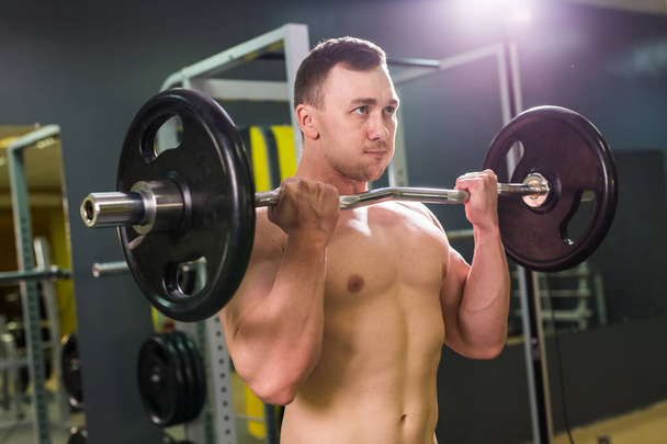 Muscular young man lifting weights in gym - Photo, Image