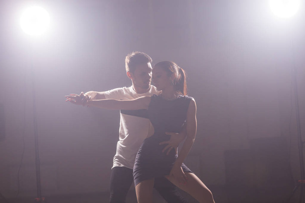 Искусные танцоры выступают в темной комнате под концертным светом и дымом. Чувственная пара, исполняющая художественный и эмоциональный современный танец
 - Фото, изображение