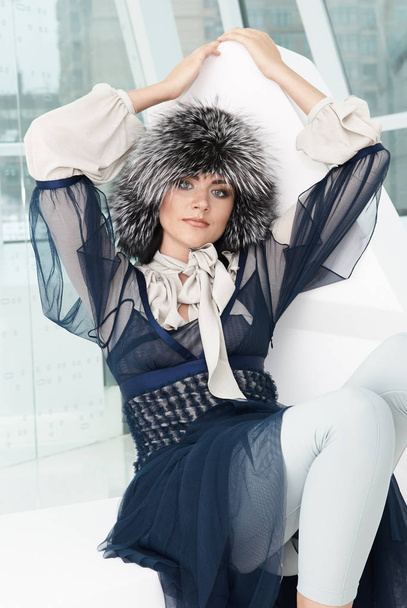 Fashion girl model posing in fur furry hat. Beautiful Woman in Luxury clothes in white interior - Fotoğraf, Görsel
