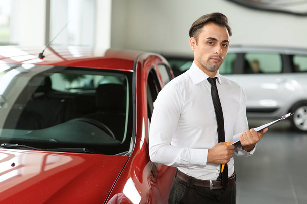 Le vendeur reste près de la voiture. Il attend des clients. La voiture est rouge. Il tient la tablette à la main
. - Photo, image