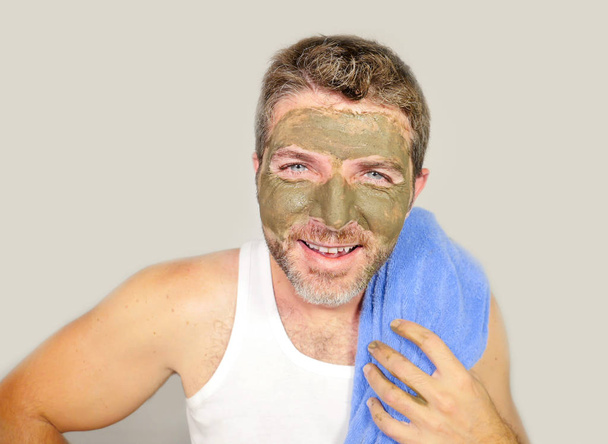 lifestyle isolated portrait of young attractive and happy man with bathroom towel  smiling with green cream on his face applying facial mask in skin care beauty and male cosmetics use concept - Foto, Imagen