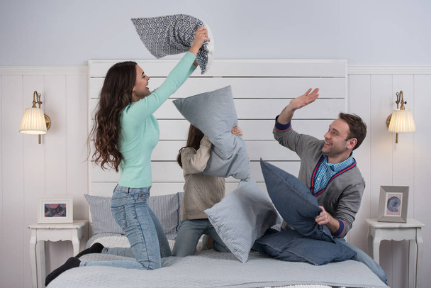 People, family concept - happy child with parents having pillow fight in bed at home - Фото, изображение